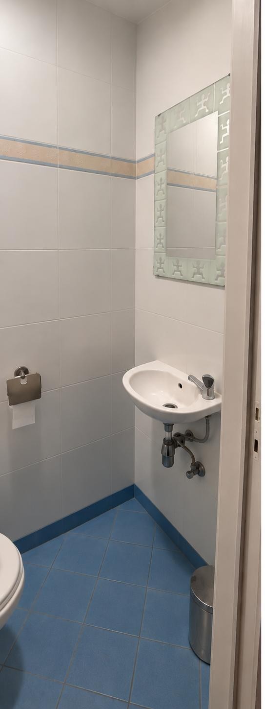 Coin lavabo avant rénovation : carrelage blanc avec frise et miroir à motifs